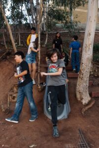 Innovations Academy students play on a slide built into a hillside in a shady tree area on campus.