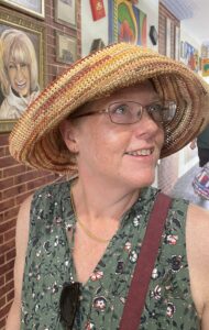 Innovations Academy Reading Specialist Jennifer Franklin looks off camera to the side wearing glasses and a multi-colored woven hat.