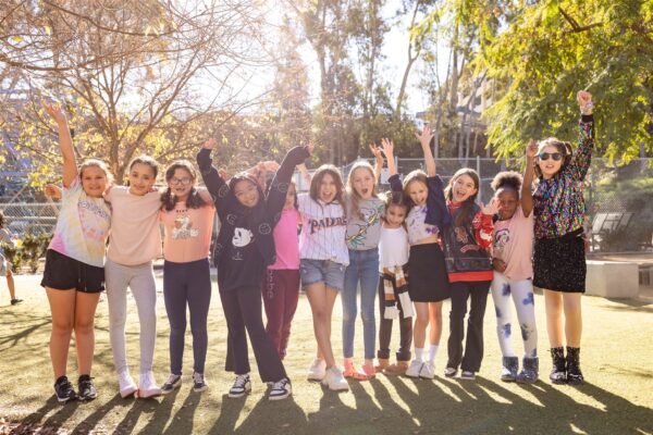 A group of Innovations Academy students stand in a line, arms outstretched and around each other’s shoulders on campus outside.